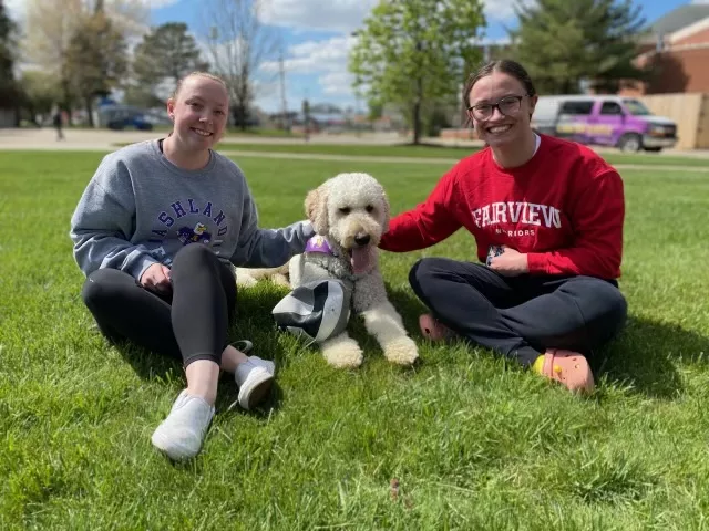 Students sitting on lawn petting a dog